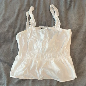 Vit ärmlös topp från H&M - Säljer en söt vit ärmlös topp från H&M i storlek XXS men stor i storleken och passar både XS och S också. Toppen har rynkade axelband och en elastisk midja för en bekväm passform. Perfekt för sommardagar eller som ett lager under en kofta. Toppen är i bra skick och redo för nya äventyr!