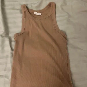 Beige ribbad linnetopp - Säljer en snygg beige ribbad linnetopp i mycket bra skick. Perfekt för sommardagar eller som ett basplagg i garderoben. Den är ärmlös och har en bekväm passform. Passar till både jeans och kjol!