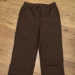Randiga kostymbyxor  - Bruna randiga kostymbyxor från NA-KD med rak passform. Använda fåtal gånger och i mycket bra skick 