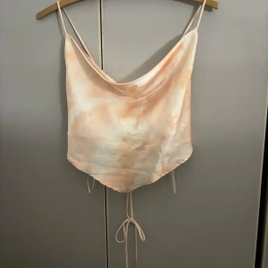 Beige satinlinne från Gina Tricot - Säljer ett snyggt beige satinlinne från Gina Tricot i storlek 38. Linnet har tunna axelband och en knytning i ryggen för en justerbar passform. Perfekt för sommarens fester eller en utekväll. Superfint och i bra skick!