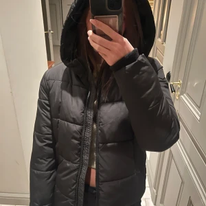 Svart pufferjacka från Pieces - Säljer en svart pufferjacka från Pieces i storlek S. Jackan har en mysig huva och stängs med dragkedja. Perfekt för kyliga dagar och håller dig varm och stilren. Använd få gånger, så den är i mycket bra skick. 