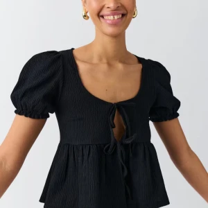 Svart topp med puffärmar - Säljer en supersöt svart topp med puffärmar och knytning framtill. Den har en luftig passform och är perfekt för både vardag och fest. Materialet är lätt och bekvämt, vilket gör den idealisk för varmare dagar. Använd 1 gång!