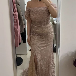 Champagne/Rosafärg  glittrig långklänning - Säljer en fantastisk champagne/rosafärgad långklänning med glittrigt mönster. Klänningen har en elegant offshoulder-design och en smickrande slits framtill. Perfekt för festliga tillfällen där du vill glänsa! ✨