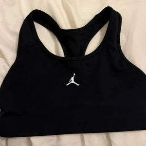 Svart sport-bh från Jordan - Säljer en svart sport-bh från Jordan i mycket bra skick. Den har en klassisk design med det ikoniska Jordan-loggan i vitt på framsidan. Perfekt för träning eller vardagsbruk. Materialet är mjukt och stretchigt för bästa komfort.