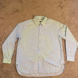 Ljusblå skjorta - Säljer en stilren ljusblå (med mint inslag) skjorta i mycket bra skick. Skjortan har en klassisk krage och långa ärmar med knappar vid ärmsluten. Perfekt för både vardag och festliga tillfällen. Passar bra till både jeans och kostymbyxor!