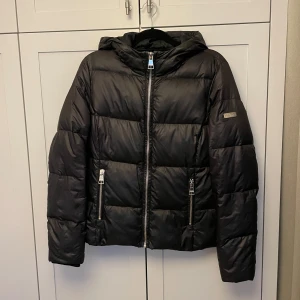 Svart pufferjacka med huva - Säljer en svart pufferjacka i mycket bra skick. Den har en praktisk huva och dragkedja framtill. 