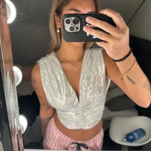 Silvrig topp - Säljer en superfin vit/silver glittrig topp som är perfekt för fest! Den är ärmlös och har en snygg omlott-design framtill. Toppen är croppad och ger en riktigt trendig look. Perfekt inför nyår. Storlek xxs men skulle säga mer som xs och s