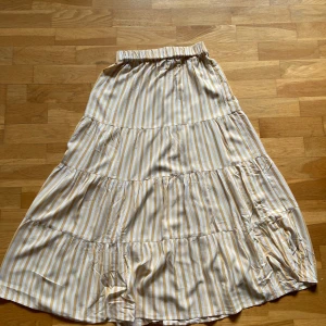 Randig långkjol från Gina Tricot - Superfin långkjol från Gina Tricot i vitt och beige med randigt mönster. Kjolens resår vid midjan är lite skruvad men går enkelt att fixa.