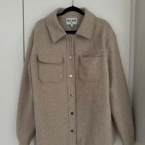 Beige jacka från NA-KD - Säljer en snygg beige jacka från NA-KD i storlek 38. Den har en stilren design med knappar framtill och två praktiska bröstfickor. Perfekt för höst och vår. 🧥✨ 