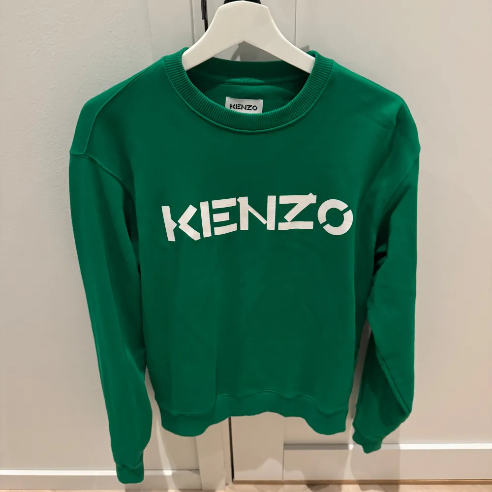 Säljer en snygg grön tröja från Kenzo i storlek S. Den har ett stort vitt Kenzo-tryck på framsidan och är i mycket bra skick. Perfekt för både vardag och chill. Passar bra till jeans eller kjol för en avslappnad look. 💚. Tröjor & Koftor.