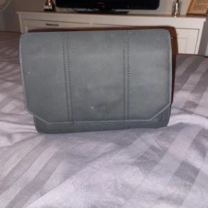 Svart axelväska i skinn - Snygg och stilren svart axelväska i skinn. Perfekt för både vardag och fest. Väskan har en justerbar axelrem och en enkel design utan onödiga detaljer. Passar till alla outfits och är ett måste i garderoben!