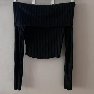 Svart ribbad offshoulder topp från Bershka - Snygg svart ribbad offshoulder topp från Bershka i storlek S. Perfekt för en kväll ute eller en stilren vardagslook. Toppen har långa ärmar och en tight passform som framhäver figuren. Tillverkad i ett mjukt och stretchigt material för extra komfort.