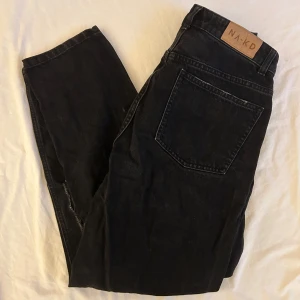 Svarta mom jeans från NA-KD - Säljer ett par svarta mom jeans från NA-KD i storlek 36. De har en cool slitning på framsidan och är perfekta för en avslappnad stil. Jeansen är högmidjade och har en bekväm passform. Perfekta för både vardag och fest!