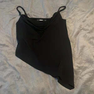 Svart asymmetrisk topp från Bik Bok - Snygg svart asymmetrisk topp från Bik Bok i storlek S. Den har tunna axelband och en unik snedskuren design som ger en cool look. Perfekt för en utekväll eller fest! 