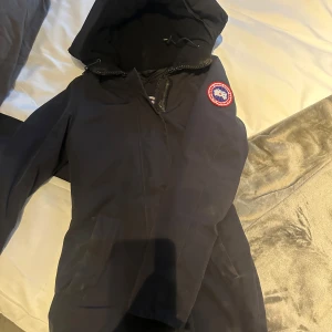Svart dunjacka från Canada Goose - Säljer en svart äkta dunjacka från Canada Goose i mycket bra skick. Jackan har en huva och är perfekt för kalla vinterdagar. Den är varm och stilren med en klassisk design. Perfekt för dig som vill hålla dig varm och snygg i vinter! ❄️ Säljer den för det inte riktigt är min stil längre!