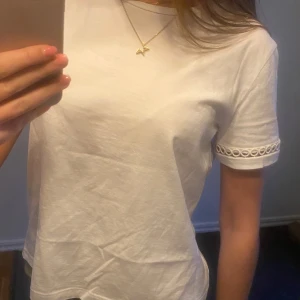 Vit t-shirt med detaljer - Säljer en superfin vit t-shirt med korta ärmar och snygga detaljer vid ärmsluten! Den är i bra skick och gjord av mjukt bomullsmaterial. Passar perfekt till jeans eller andra byxor🤍