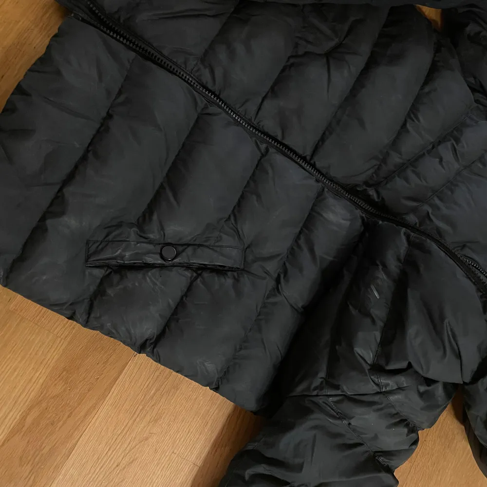 Säljer en svart puffer jacka från Nike i bra skick. Jackan har en skön huva och dragkedja framtill. Perfekt för kalla dagar med sin pufferdesign som håller värmen. Den har praktiska fickor med knappar. Passar både till vardags och sportiga aktiviteter. 13-15 år. Jackor.