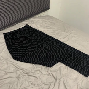 Svarta randiga kostymbyxor  - Säljer ett par snygga svarta byxor med vita ränder. De har en loose passform och är perfekta för både vardag och fest. Byxorna är i mycket bra skick och har en hög midja som ger en bekväm och stilren look. Perfekta för höst och vår!