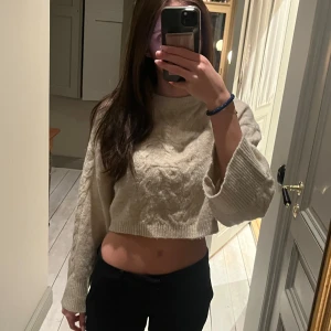 Beige stickad croppad tröja - Superfin beige stickad tröja från H&M,  den är croppad och perfekt året runt. Den har ett snyggt mönster och långa ärmar, vilket gör den både stilren och mysig. Passar perfekt till ett par jeans eller kjol för en avslappnad look. 56% akryl, 23% polyamid, 12% ull, 5% alpacka, 4% elastan. 