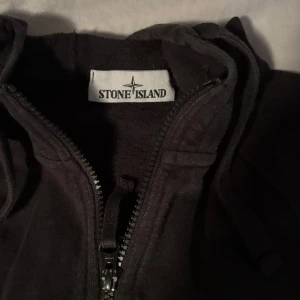 Svart zip Hoodie från Stone Island - Säljer en svart zip hoodie från Stone Island i bra skick. Den har en dragkedja framtill och är långärmad. Perfekt för höst och vår, med en stilren look som funkar till det mesta. Jackan är gjord i ett mjukt material som känns skönt mot huden.