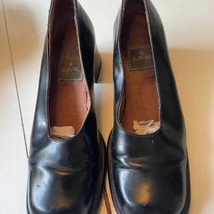 Svarta klackskor från J.P.W. - Säljer ett par svarta klackskor från J.P.W. i bra skick. Skorna har en robust klack och en rundad tå, vilket ger dem en klassisk look. Perfekta för både vardag och fest. De är gjorda i skinn och har en bekväm passform.