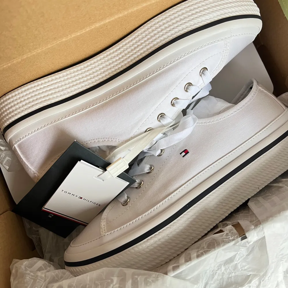 Säljer ett par snygga vita sneakers från Tommy Hilfiger i nytt skick. De har en klassisk design med snörning och en liten logga på sidan. Perfekta för vår och sommar, och passar till nästan alla outfits. Skorna är i storlek dam 39 och kommer i originalförpackning.. Skor.