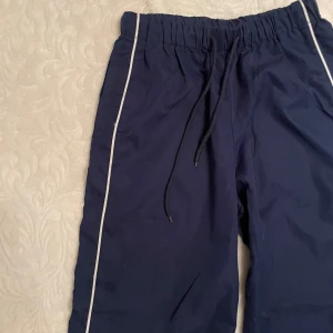 Mörkblå byxor med vita ränder - Säljer ett par mörkblå byxor i storlek XS. De har en loose passform med vita ränder längs sidorna och en bekväm resårmidja med snörning. Perfekta för en avslappnad stil eller träning. 🏃‍♀️
