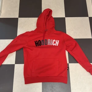 Röd hoodie från Hoodrich - Säljer en snygg röd hoodie från Hoodrich i storlek S. Den har en stor ficka fram och texten 'HOODRICH' . Perfekt för en casual look eller att mysa i hemma. Grym kvalitet och superbekväm! Köptes på JD sports i Stockholm för 899kr för drygt 2 år sedan men den kommer inte till lika mycket användning som jag trodde. Priset kan diskuteras !