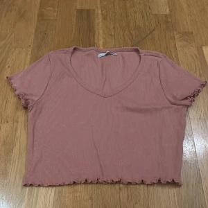 Rosa ribbad topp från 157 - Säljer en söt rosa ribbad topp från 157 i storlek M. Den har en v-ringad hals och korta ärmar med volangdetaljer vid ärmslut och nederkant. Perfekt för sommardagar eller en avslappnad stil. 🩷