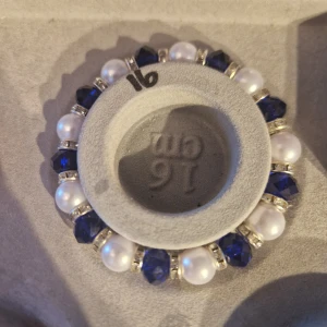 Blått och vitt armband med pärlor - Snyggt armband med vita pärlor och blå facetterade pärlor. Armbandet har också små silverfärgade detaljer mellan pärlorna. Perfekt för att ge en elegant touch till din outfit, oavsett om det är till vardags eller fest.