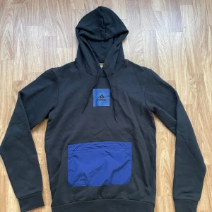 Ny Adidas Hoodie - Helt ny, oanvänd autentisk Adidas-hoodie | Prislapp ingår | Storlek S | Blå tryck på tröjan, ficka med blixtlås | Originalpris 579:-