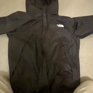 Säljer en svart vindjacka från The North Face i mycket bra skick. Jackan har en huva och dragkedja framtill, perfekt för blåsiga dagar. Den är stilren och enkel att matcha med olika outfits. Passar både till vardags och utomhusaktiviteter.