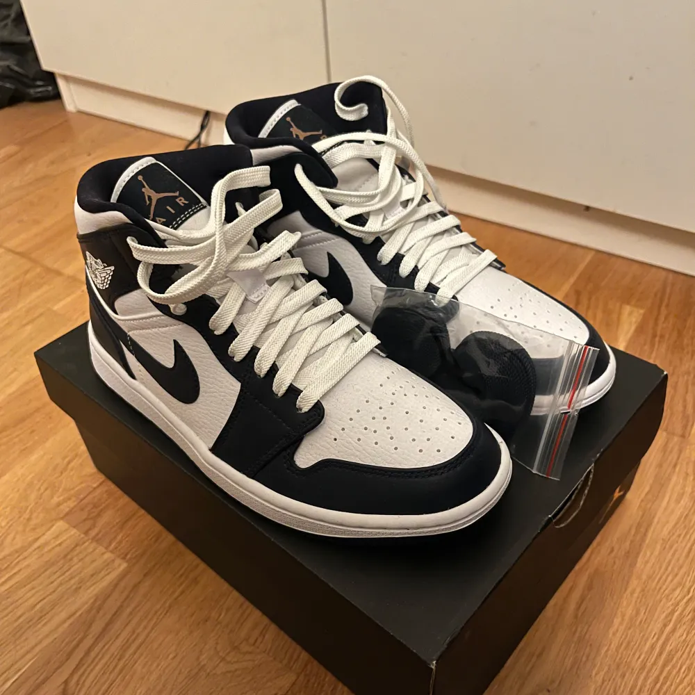 Säljer dessa helt oanvända Nike Air Jordan 1 Mid i svart/ blå och vit. Skorna är i nytt skick och kommer med extra svarta skosnören. Skorna är i storlek 40 men passar även 39 och är helt oanvända. Passa på att köpa dessa snygga sneakers!. Skor.