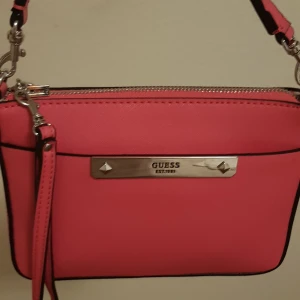 Väskor  - Jag säljer min fina väska Guess axelväska, mycket bra skick använd 2gånger Inga skador ej smutsig, men stått i garderoben ett bra tag,,,,Hör av dig vid intresse 