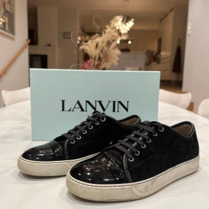Svarta sneakers från Lanvin - Säljer ett par snygga svarta sneakers från Lanvin i mycket bra skick. Skorna har en stilren design med en kombination av skinn och mocka, samt klassisk snörning. Perfekta för både vardag och festliga tillfällen. Kommer med originalförpackning.