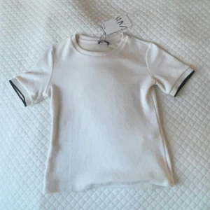 Stickad t-shirt med detaljer på armarma - Oanvänd, prislapp kvar. Ljusbeige/Vit