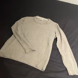Stickad tröja från Selected Homme - Säljer en stilren stickad tröja från Selected Homme. Perfekt för kyligare dagar. Den ribbade strukturen ger en snygg och look. Den ser ganska grå ut på bilderna men den är mer åt beigea hållet. Väldigt bra skick utan defekter. Står S men sitter mer som M.