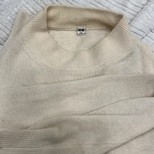 Beige stickad tröja från Uniqlo - Mysig beige stickad tröja från Uniqlo med ribbad krage och ärmslut. Perfekt för kyliga dagar och enkel att matcha med olika outfits.