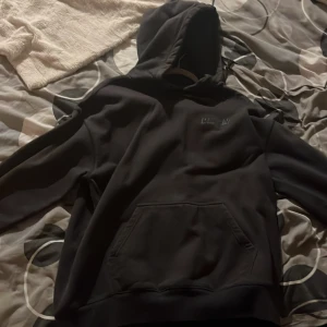 Svart hoodie från DR. DNM - Säljer en svart hoodie från DR. DNM med en klassisk design och känguruficka framtill. Perfekt för en avslappnad stil med en bekväm huva.