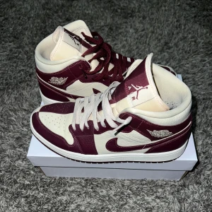 Nike Air Jordans  - Snygga Nike Air Jordans i en stilren kombination av vinrött och vitt. Skorna har klassisk snörning och är tillverkade i skinn. Perfekta för dig som vill ha en sportig och trendig look.