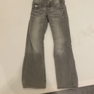Grå jeans från Gina Tricot - Snygga grå jeans från Gina Tricot i storlek 146. De har en klassisk femficksdesign med dubbla knappar i midjan och en bootcut-stil. Perfekta för en avslappnad look.