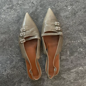 Spetsiga ballerina från Vagabond - Eleganta ballerinaskor med spetsig tå och tre dekorativa spännen. Skorna har en smal rem runt hälen för extra passform. Använda fåtal gånger, mycket gott skick. Brungrå i färgen. 