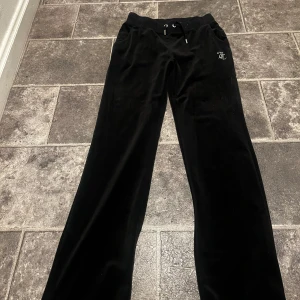 Svarta mjukisbyxor från Juicy Couture - Snygga svarta mjukisbyxor från Juicy Couture med glittrig text på baksidan. Byxorna har en bekväm passform med dragsko i midjan för justerbarhet. Perfekta för en avslappnad stil. Aldrig använt och köparen står för frakten. 
