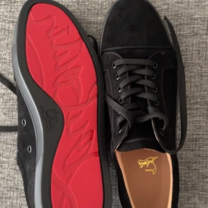 Loubutins - Snygga svarta sneakers i mocka med den ikoniska röda sulan från Christian Louboutin. Skorna har snörning och en stilren design som passar perfekt för en trendig look. Plus dem är bara använda 2-3 gånger för dem va inte direkt min stil. Dessa är också a kopierade 