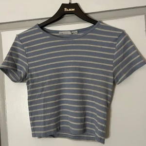 Blå och vit randig topp från 157 - Säljer en blå och vit randig topp från 157 i storlek M. Toppen har korta ärmar och en rund halsringning. Perfekt för en avslappnad stil.