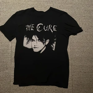 Svart T-shirt med The Cure-tryck - Säljer en svart T-shirt med ett coolt tryck av The Cure på framsidan