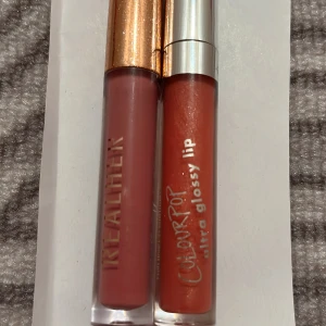 Två läppglans från ColourPop och RealHer - Säljer två läppglans. Ett från ColourPop i en skimrande orange nyans med silverlock och texten 'ultra glossy lip'. Det andra från RealHer i en matt liquid lipstick birthday edition 3 ml. Perfekt för att ge läpparna en glansig eller matt finish. Båda 50kr