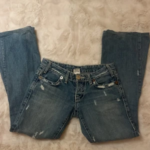 Blå jeans från True Religion - Säljer ett par blå jeans från True Religion med slitna detaljer och broderade bakfickor. Jeansen har en klassisk femficksdesign och är tillverkade i USA. Perfekta för en avslappnad stil. Midjemått rakt över är 36, innerbenslängd är 73 och totallängd är 95🩷😘