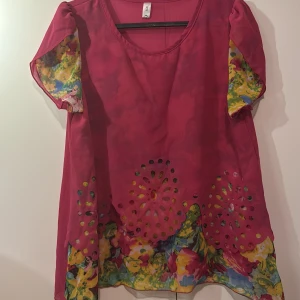 Rosa blommig blus med hålmönster - Säljer en färgglad rosa blus från TXL i storlek XXL. Blusen har korta ärmar med blommigt mönster och dekorativa hålmönster framtill. Perfekt för en somrig look!