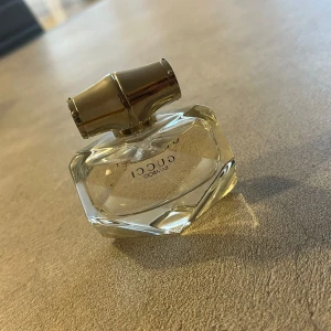 Gucci Bamboo parfym - Elegant parfymflaska från Gucci Bamboo med en unik, facetterad design. Flaskan är genomskinlig med en metallisk kork i silverfärg. Perfekt för den som söker en sofistikerad doftupplevelse. Sprejat några gånger den är nästan ny
